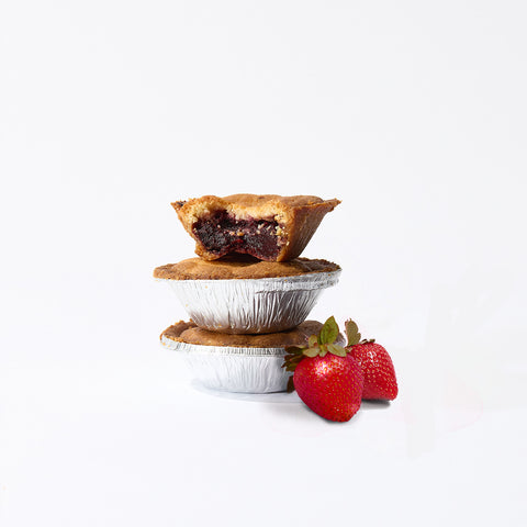 Two stacked No Guilt Bakes Low Carb Tarts, with one on top bitten to reveal a fruit filling, accompanied by two strawberries, all set against a plain white background. Each tart from the Low Carb Tart Bundle contains just 3g net carbs and no added sugar.