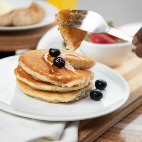 A person eating a stack of pancakes from the No Guilt Bakes Regular Bread Bundle, topped with blueberries and syrup.