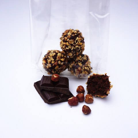 Bag of Hazelnut and Chocolate Snowball from No Guilt Bakes, featuring chocolate truffles coated in nuts, alongside pieces of dark chocolate and whole hazelnuts.