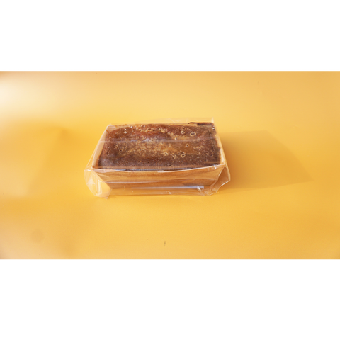 A rectangular loaf of No Guilt Bakes' Sticky Toffee Keto Cake Loaf, wrapped in plastic, rests on a yellow background, providing a savory alternative to sugar-laden desserts.