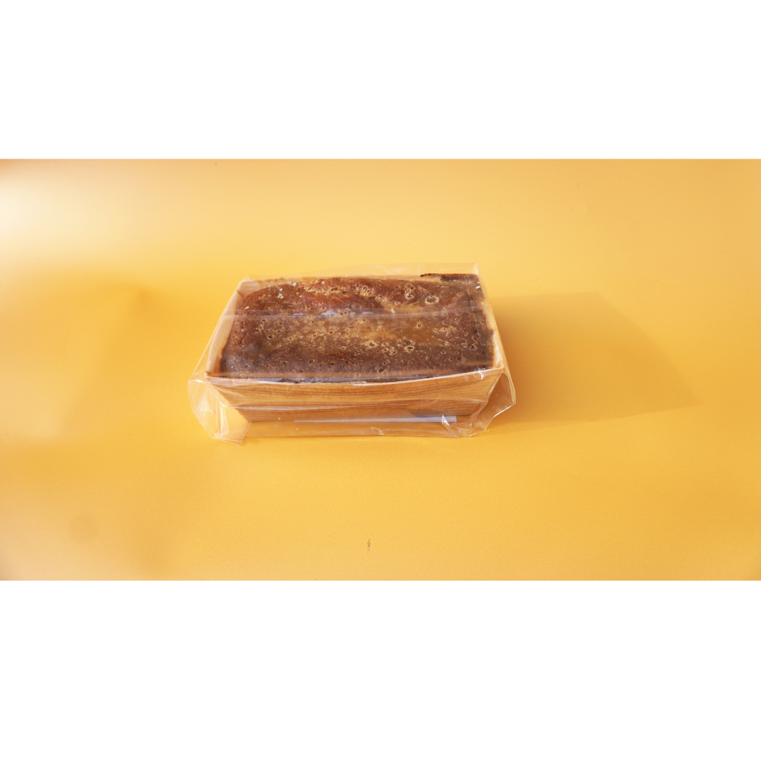 A rectangular loaf of No Guilt Bakes&#39; Sticky Toffee Keto Cake Loaf, wrapped in plastic, rests on a yellow background, providing a savory alternative to sugar-laden desserts.