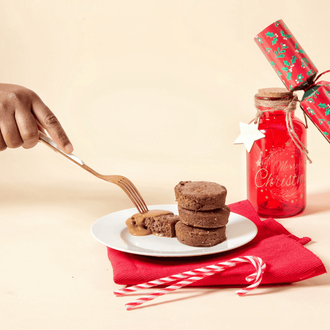 A person holding a fork next to a plate of No Guilt Bakes' Sticky Toffee Keto Cake Bite | Limited Edition.