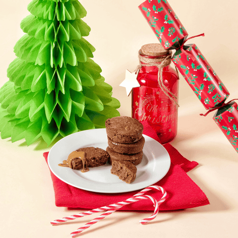 A plate of No Guilt Bakes Sticky Toffee Keto Cake Bite Limited Edition next to a Christmas tree.