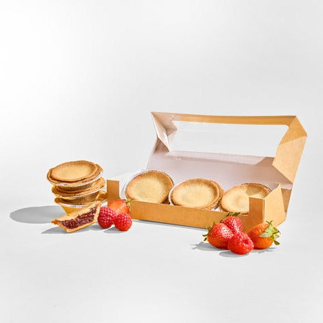 A partially open box reveals No Guilt Bakes' gluten-free plain tarts, accompanied by low-carb Strawberry Tarts (Keto) from the same brand, and whole strawberries artfully arranged around it against a white background.